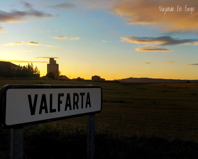 Cartel de Valfarta a la entrada del pueblo con el sol poniéndose en el horizonte.